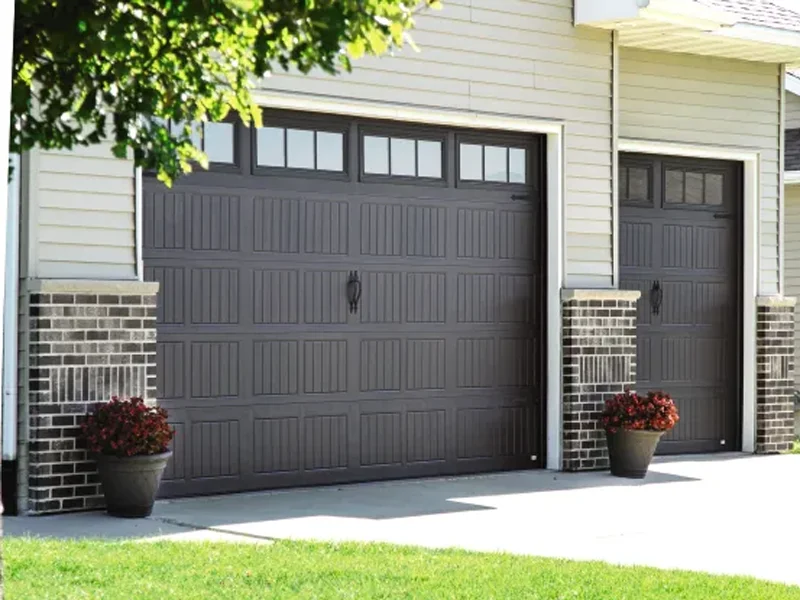Dark brown garage doors with windows, flanked by decorative brick columns and flower pots, showcasing residential garage design.