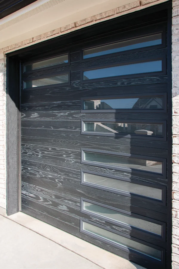 Modern black garage door with horizontal wood grain design and glass panels, showcasing a stylish and functional solution for residential properties, reflecting the services of Overhead Door Company of Fresno.