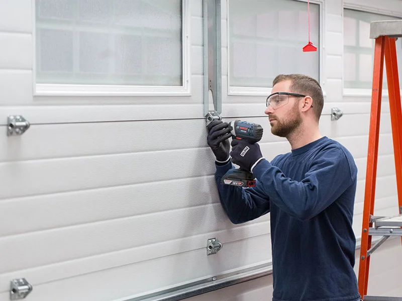 Technician installing garage door hardware using a power drill, showcasing professional service for residential garage door maintenance and upgrades.