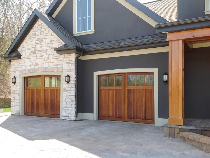 Elegant wooden garage doors on a modern home with stone and dark exterior, showcasing quality garage door solutions for residential needs.