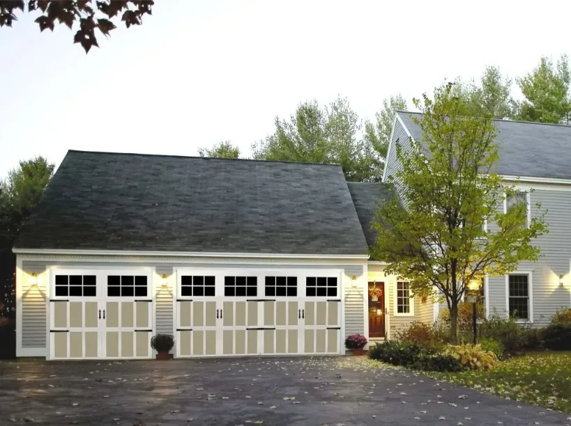 Carriage house-style garage doors on a residential home, showcasing traditional design with multiple panels and windows, surrounded by landscaping and warm exterior lighting.