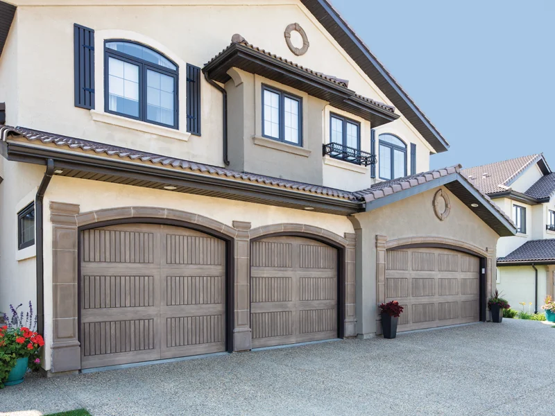 Modern home exterior with three wooden garage doors, decorative windows, and landscaped entrance, showcasing Overhead Door Company of Fresno's garage door installation services.