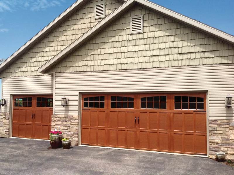 Garage with two wooden garage doors featuring window panels, stone accents, and a well-maintained exterior, representing Overhead Door Company of Fresno's quality garage door solutions.