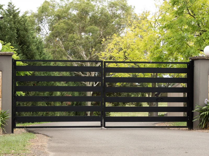 Black horizontal slatted gate installed for secure property access, surrounded by greenery, showcasing durability and integration with landscape.
