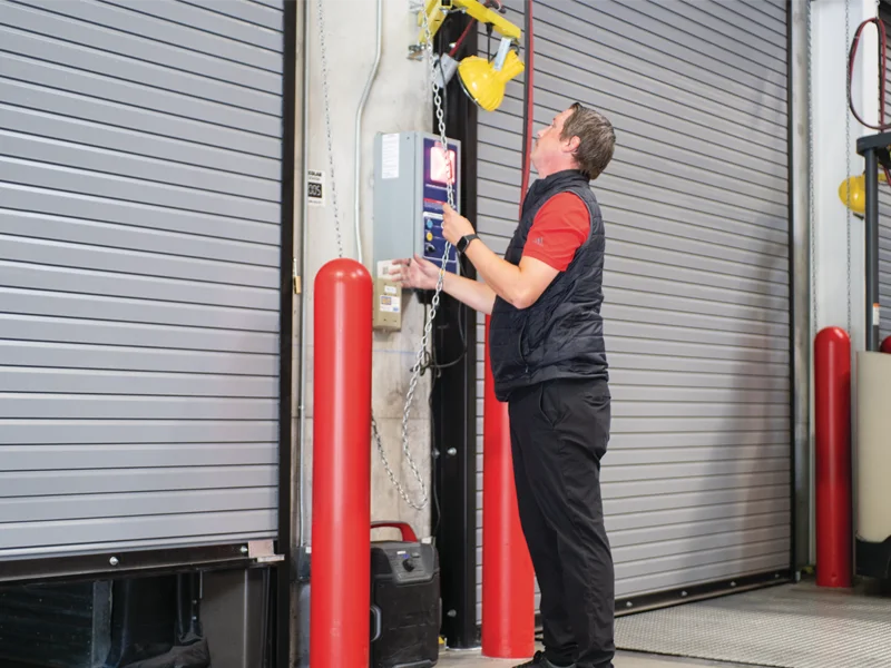 Technician operating a heavy-duty rolling steel garage door control panel in a commercial setting, emphasizing installation and maintenance services.