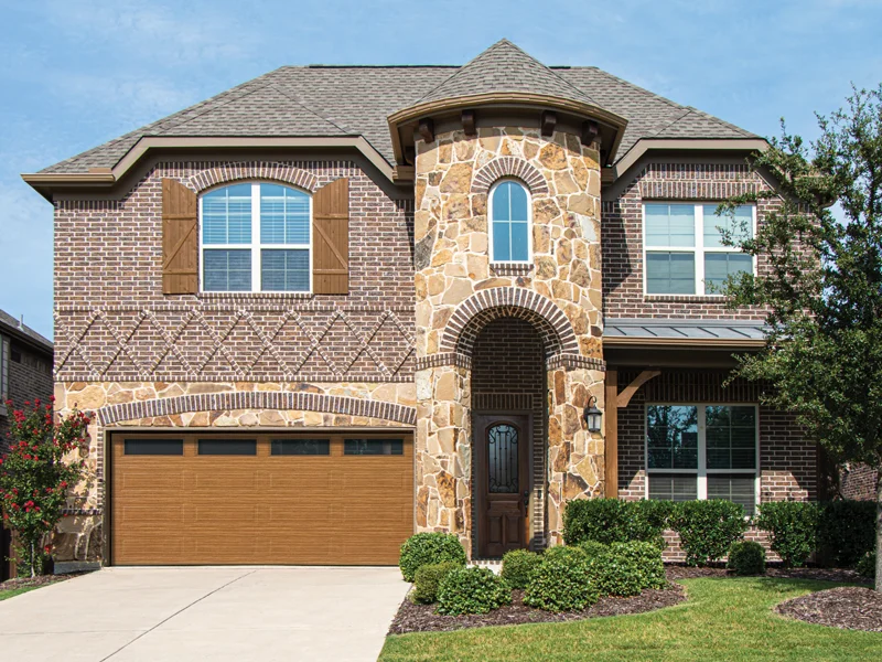 Residential home exterior featuring a stylish garage door, stone and brick facade, landscaped front yard, and modern architectural design, reflecting quality garage door installation services by Overhead Door Company of Fresno.