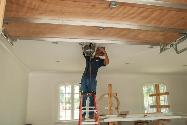 Technician repairing garage door opener on ladder, ensuring safety and functionality for residential garage door systems.