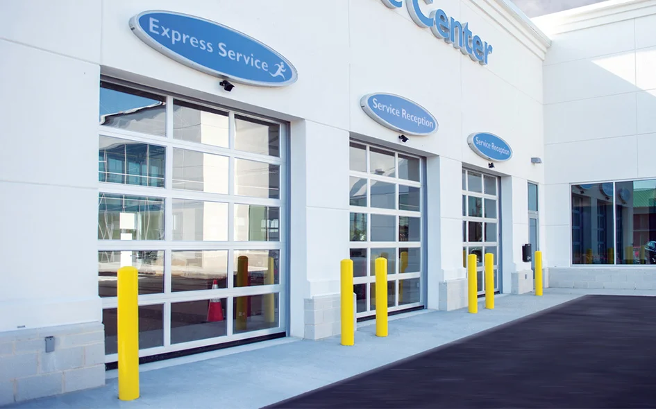 Aluminum glass door installation at a service center, featuring multiple glass panels and yellow safety bollards, highlighting commercial application and accessibility.