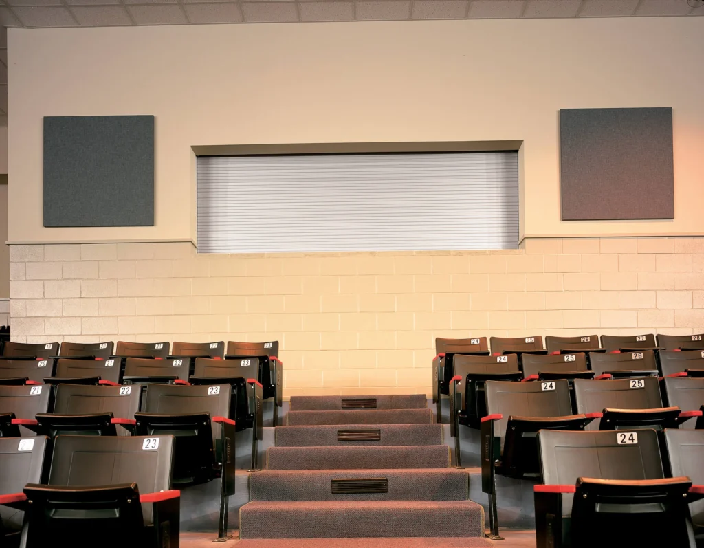 Rolling counter door in a commercial setting above theater seating, featuring a sleek design and integrated frame, with adjacent sound-absorbing wall panels.