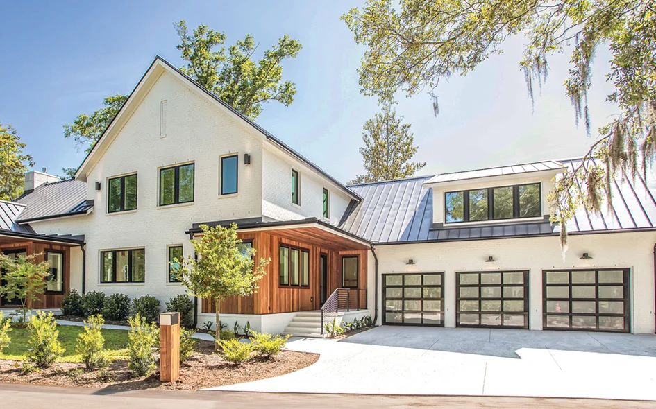 Modern home exterior featuring aluminum glass garage doors, sleek design, and a contemporary aesthetic, surrounded by landscaped greenery.