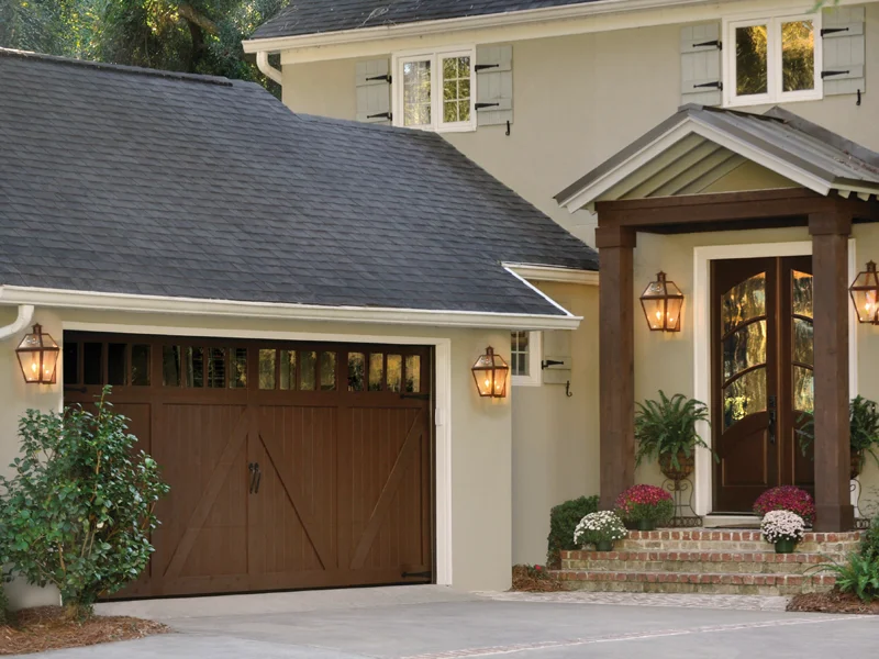 Garage door with wooden design and windows, adjacent to a modern home entrance featuring decorative lanterns and landscaping, illustrating professional garage door service and maintenance in Fresno, CA.