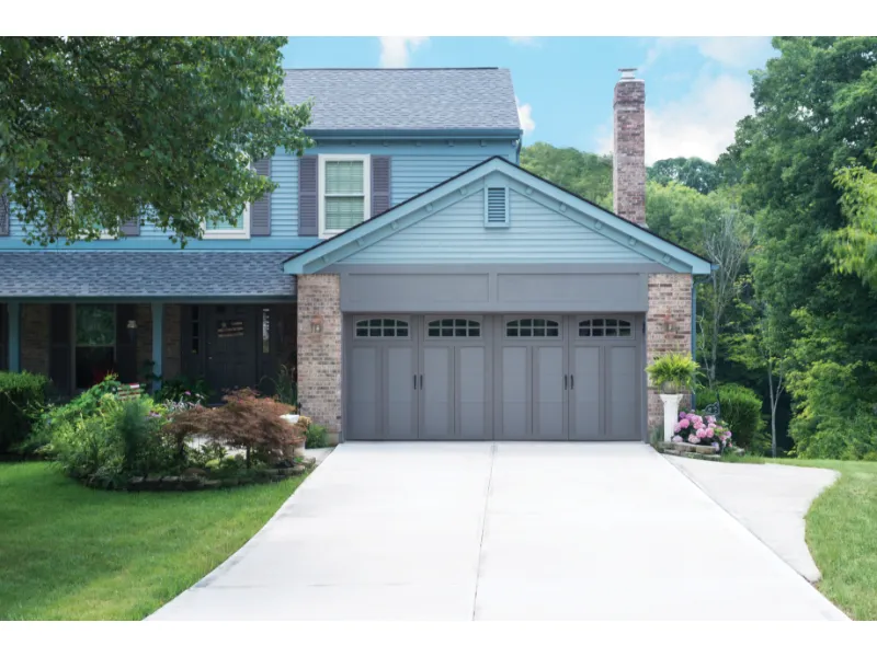 Modern garage door installation in residential setting, featuring gray Impression Steel doors, surrounded by landscaped yard and brick accents.