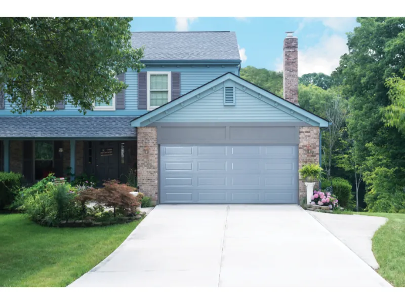 Modern gray garage door on residential home, surrounded by green landscaping and brick accents, showcasing transformation for garage door installation.