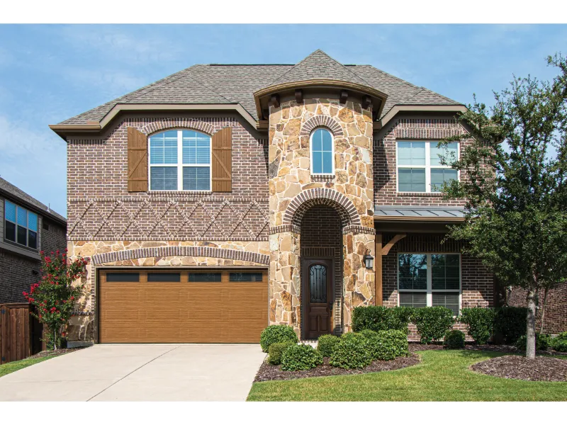 Traditional steel garage door installation on a residential home with stone and brick exterior, featuring a landscaped yard and driveway.