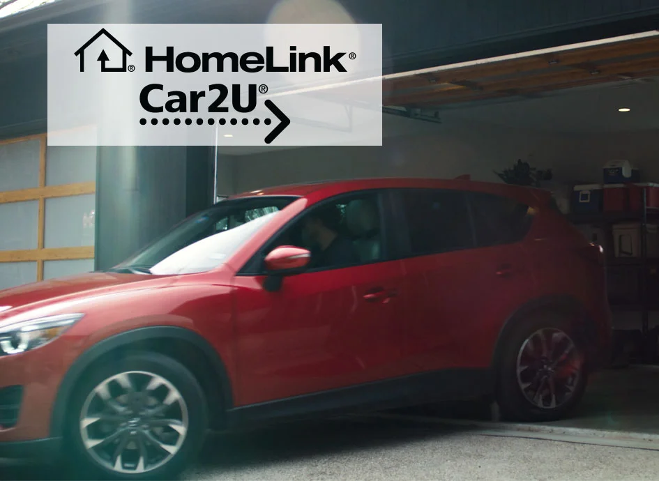 Red car equipped with HomeLink Car2U® technology entering a garage, showcasing the integration of home automation and garage door access systems.