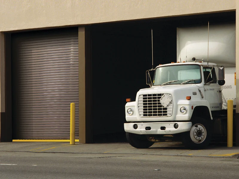 Truck with a white cab parked near a roll-up door of a loading dock, highlighting truck trailer and box truck door services for commercial fleets.